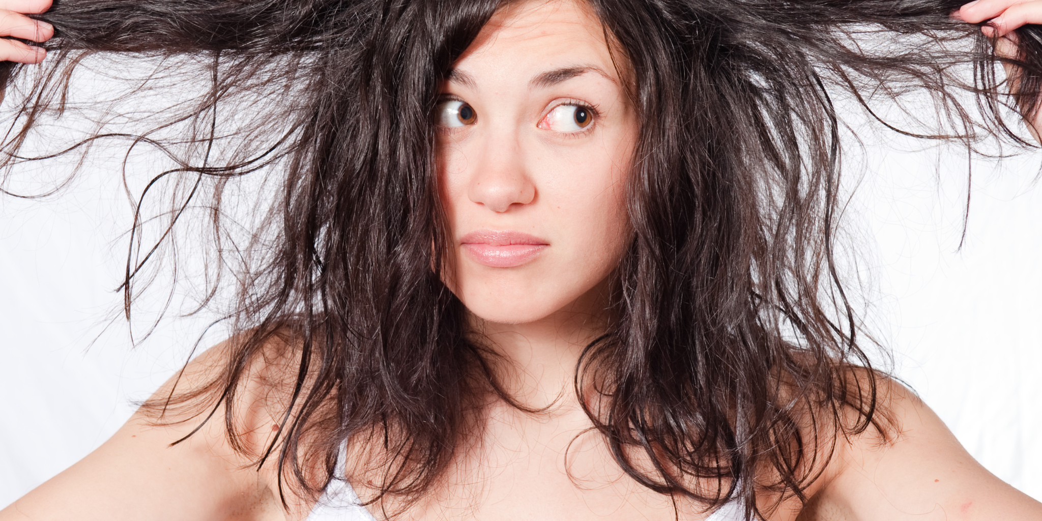 Woman holding dry damaged hair showing split ends and brittle strands