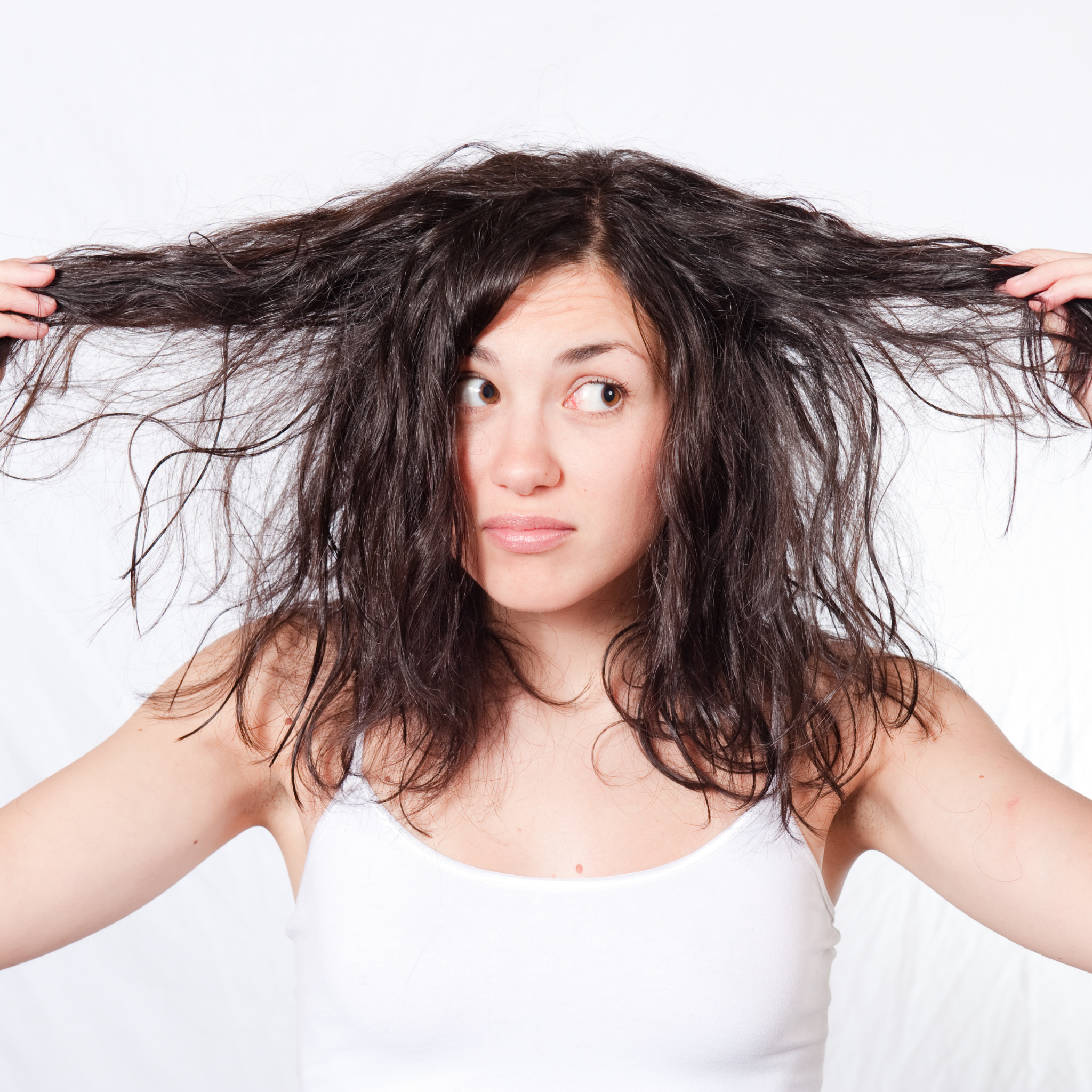 Woman holding dry damaged hair showing split ends and brittle strands