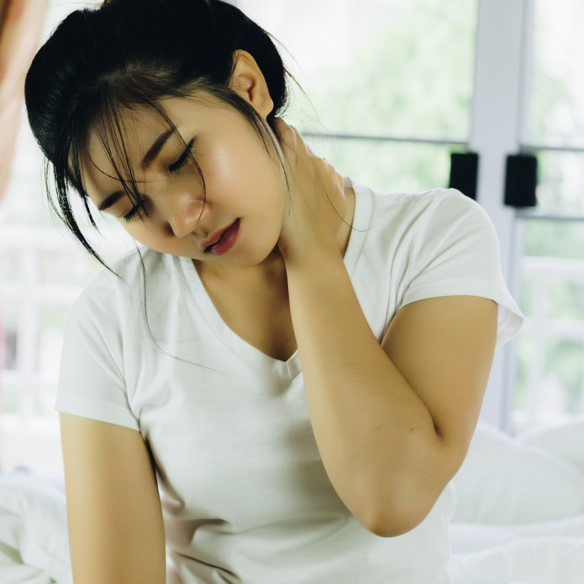 asian woman in white t-shirt rubbing neck