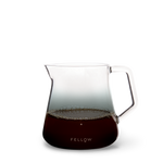 Clear glass coffee pitcher with handle, filled with coffee, on a white background. Brand 'Fellow' visible.
