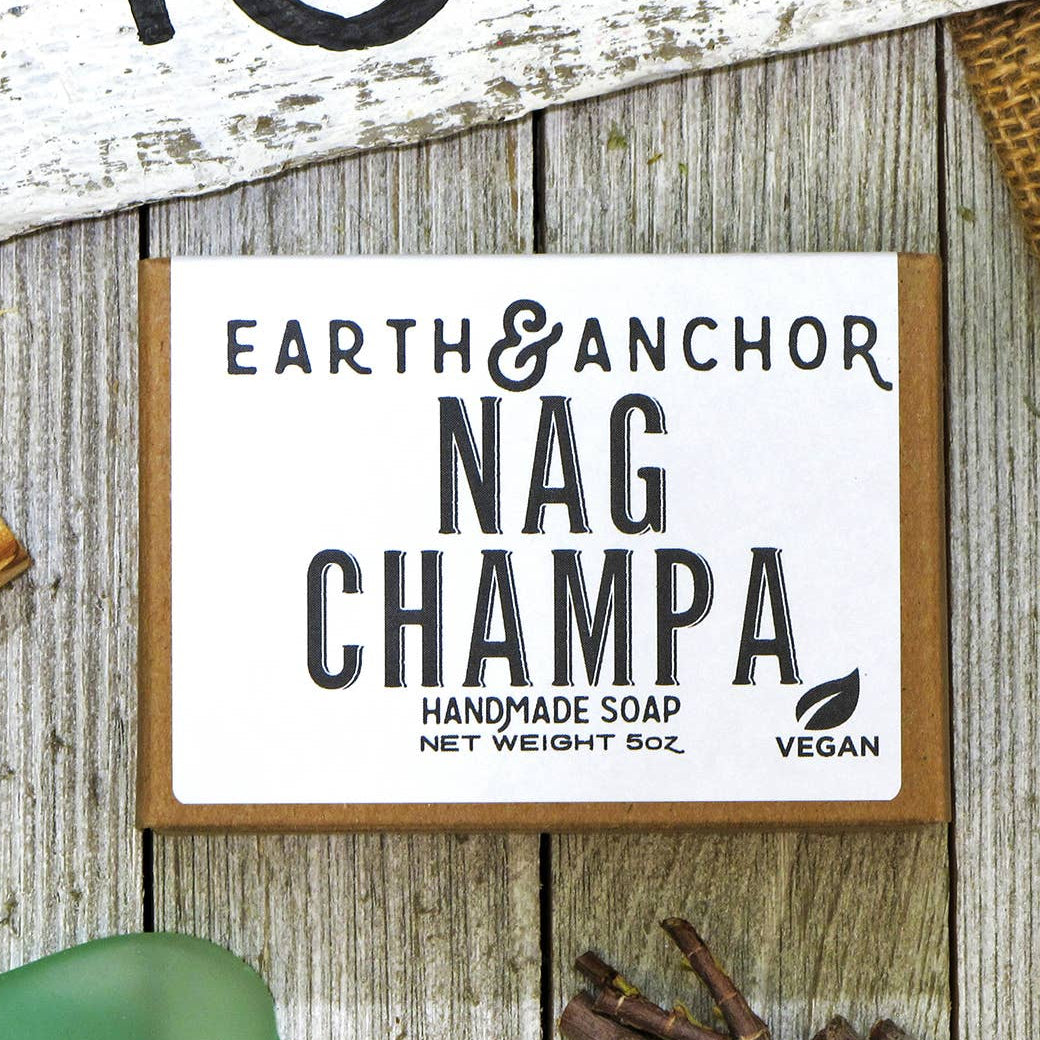 A packaged bar of handcrafted soap labeled 'Nag Champa' from Earth & Anchor, displayed on a wooden surface with decorative elements around it.