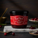 Jar of 'Eat This Yum! Heirloom Cranberry Compote' on a dark background with cranberries and a spoon.
