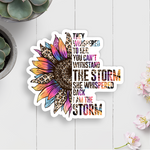 Colorful sunflower-themed sticker with motivational quote on a white wooden surface with plants.