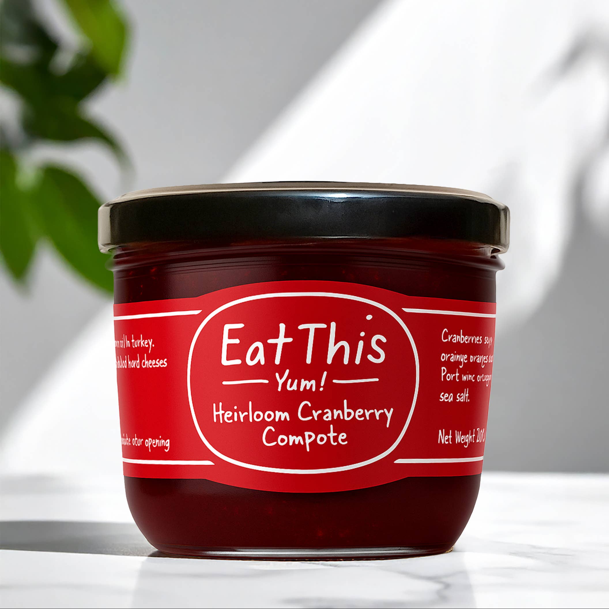 Jar of Heirloom Cranberry Compote with 'Eat This Yum!' label on a white surface.