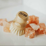 Wooden dish brush with 'Zefiro' branding on a white background with pinkish-orange crystals.