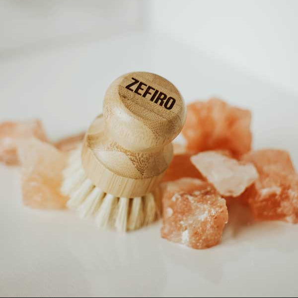 Wooden dish brush with 'Zefiro' branding on a white background with pinkish-orange crystals.