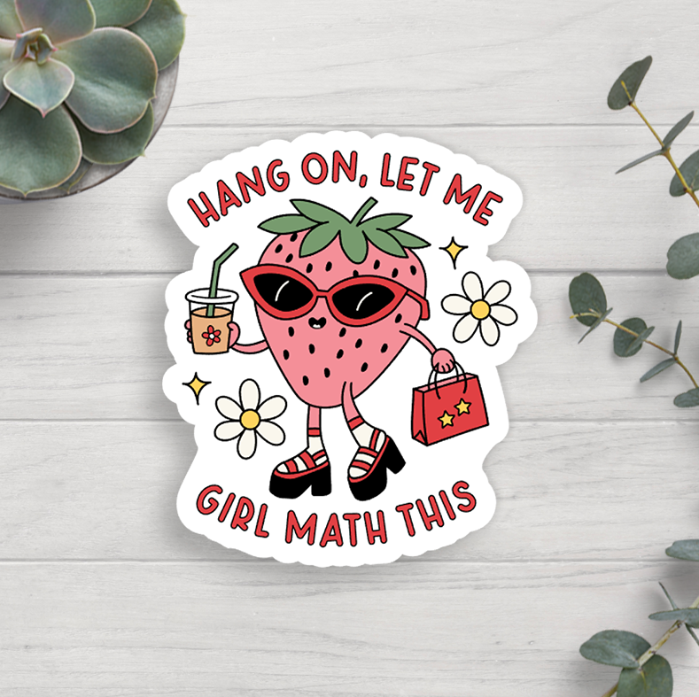 A vinyl sticker with a strawberry and girl math symbols, placed on a white surface with a plant and decorative items around it.