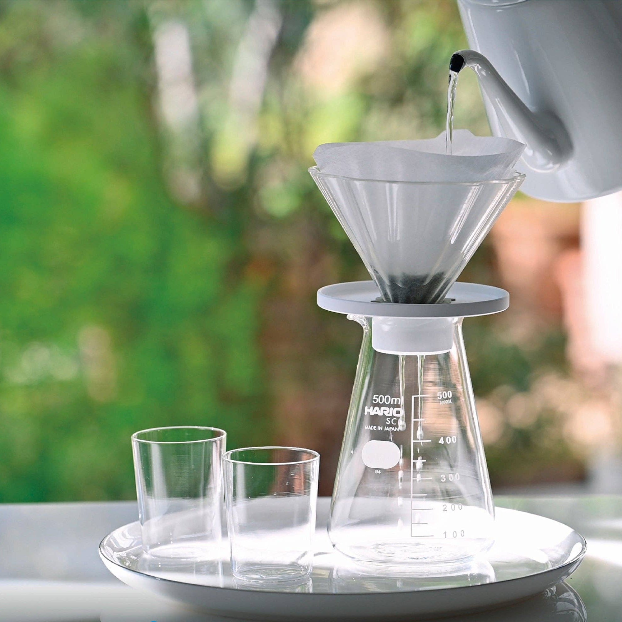 Coffee brewing process using a Hario coffee maker with a blurred outdoor background