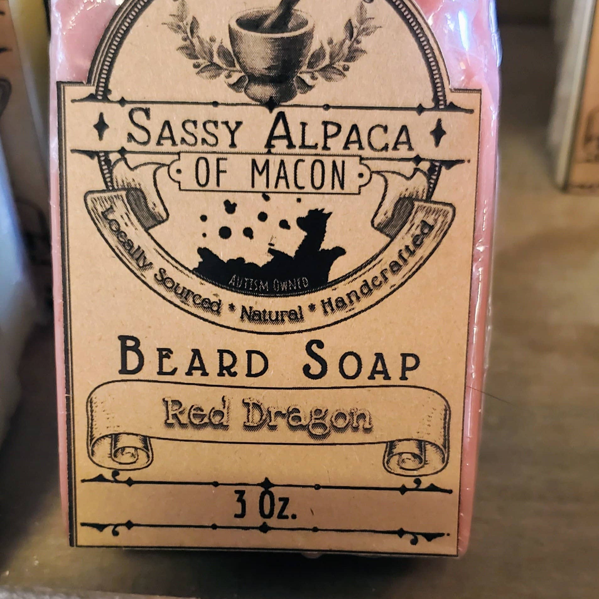 Beard soap packaging with 'Sassy Alpaca of Macon' branding on a wooden surface.