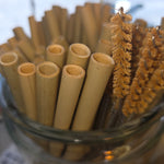 Bamboo straws in a clear glass container with a brush in the background.