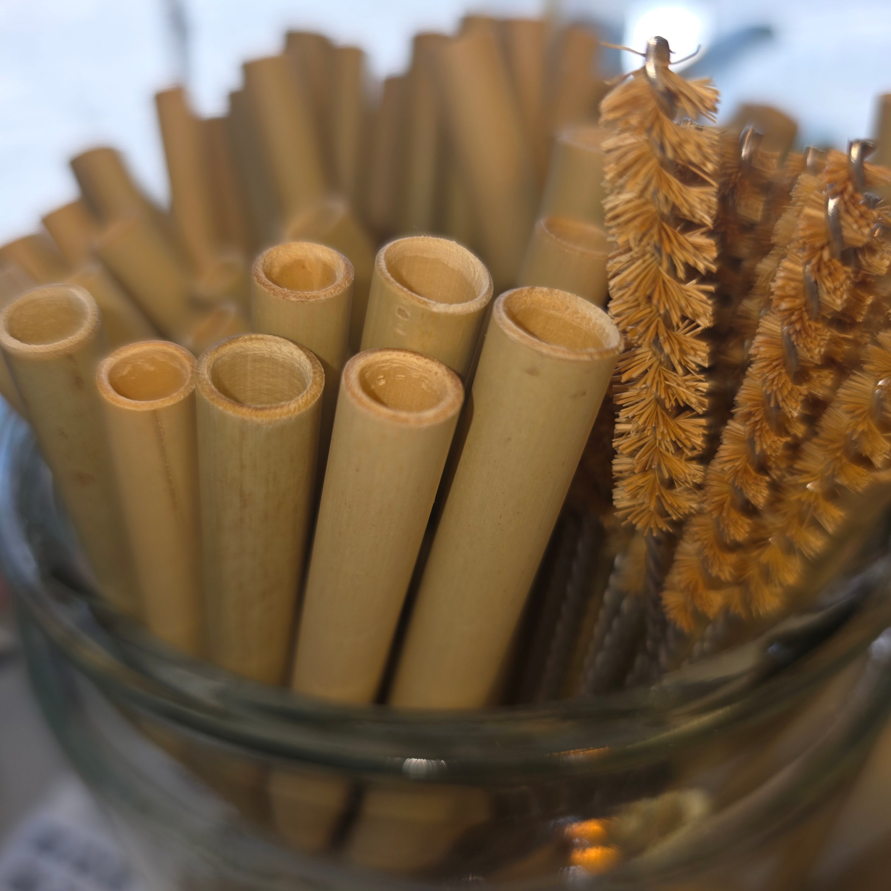 Bamboo straws in a clear glass container with a brush in the background.