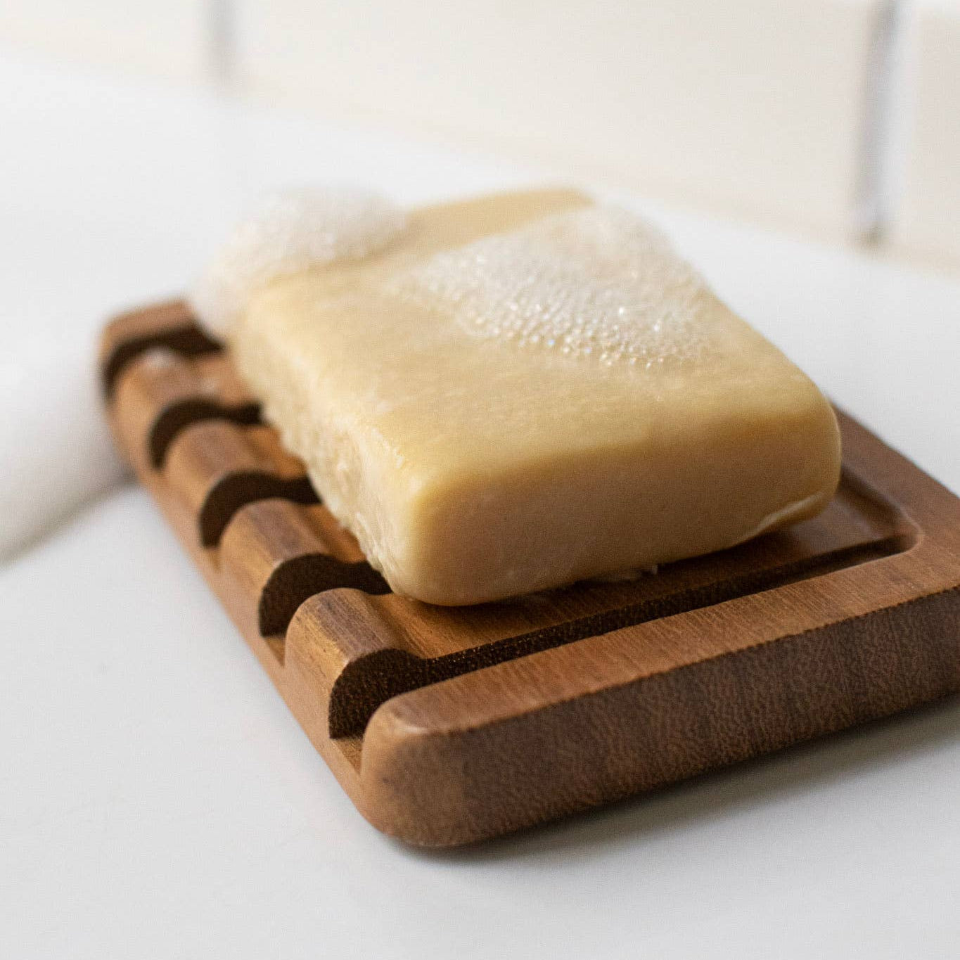 Bar of soap on a teak wood soap dish with a blurred background