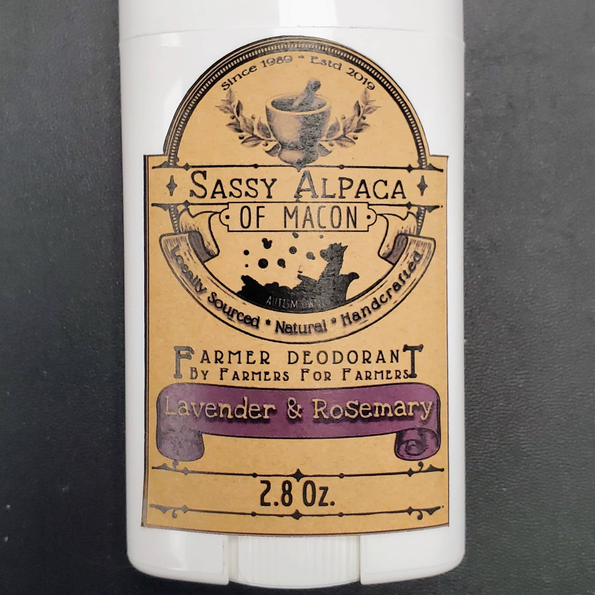 Deodorant stick with 'Sassy Alpaca of Macon' label on a dark background