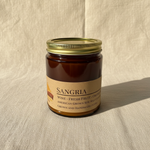 Sangria soy candle in amber apothecary jar on warm cream linen background with shadow
