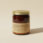 Sunday Brunch soy candle in amber apothecary jar on warm cream linen background with shadow