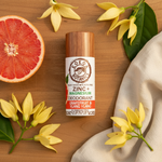 Grapefruit & Ylang Ylang magnesium deodorant flat lay on wood surface with halved grapefruit and ylang ylang flowers