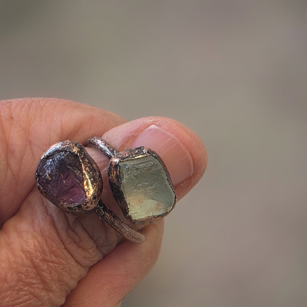 Actual raw purple and green fluorite adjustable ring on a copper band, held in hand, with a softened background