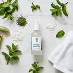 Peppermint Magnesium Oil Spray – flat lay on white marble with peppermint sprigs, magnesium flakes and jade roller