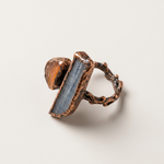 Raw ruby and kyanite adjustable ring lying on its side, showing the elongated blue kyanite blade and smaller amber stone