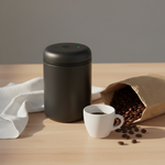 Fellow Electric Atmos vacuum canister matte black on wood surface with specialty coffee beans and espresso cup