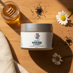 Black Seed & Honey Whipped Body Butter flat lay on warm wood with raw honey, black seeds and chamomile