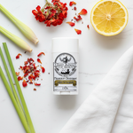 Light in August magnesium deodorant flat lay on white surface with lemongrass, geranium petals and lemon