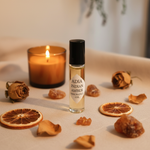 Adia Indian Amber Fragrance Oil styled with amber candle, dried roses, and raw amber resin on cream linen