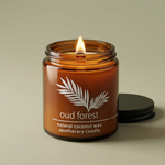 Hemlock Park Oud Forest 4 oz amber candle with a lit wood wick and ridged black lid on a smoky olive background