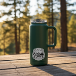 Camping Because Therapy Is Expensive vinyl sticker on a dark green tumbler outdoors with pine trees