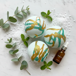 Eucalyptus and mint bath bombs on white marble with fresh eucalyptus sprigs, mint leaves, and epsom salt