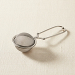 Stainless steel snap mesh tea ball infuser with scissor handle on warm linen background