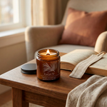Lit Foxtail Fir coconut wax candle with a ridged black lid on a wooden side table in a cozy autumn reading nook