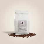 Apothecary Beans Rwanda white coffee bag on warm off-white background with coffee beans scattered at base