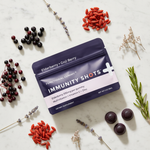 Immunity Shots Elderberry & Goji Berry – lifestyle flat lay with elderberries, goji berries, and botanicals on white marble