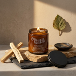 Lit Smoked Palo Santo candle with a black lid on layered limestone and slate with sculptural wood accents