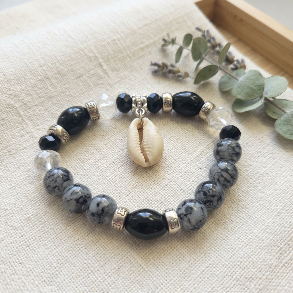 Black and gray beaded stretch bracelet styled on ivory linen with a sage botanical accent