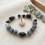 Black and gray beaded stretch bracelet styled on ivory linen with a sage botanical accent