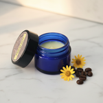 Bright Eyes Under Eye Cream cobalt blue jar on white marble vanity with arnica flowers and coffee beans in soft morning light