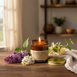 Prairie Spring candle lit on wooden surface with lilac sprigs and honeysuckle