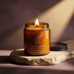 Hemlock Park Frankincense amber candle with a ridged black lid on travertine against a smoky plum backdrop