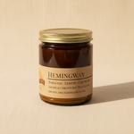Hemingway soy candle in amber apothecary jar on warm cream linen background with shadow