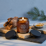 Lit Sierra Solstice candle with a black lid on layered limestone and slate with cedarwood and golden resin accents