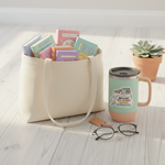 Brings Books Everywhere vinyl sticker on a travel mug next to a canvas tote overflowing with books