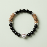 Black beaded baseball bracelet with white baseball accents and tan chip details on a pale sage background