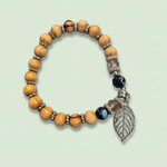 Tan wood bead bracelet with silver-tone leaf charm on a pale sage background