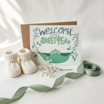 Welcome Little Sweet Pea baby card with tiny booties, baby's breath flowers and green ribbon on soft white surface