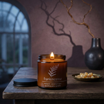 Lit Frankincense apothecary candle on a dark walnut table in an atmospheric autumn twilight setting