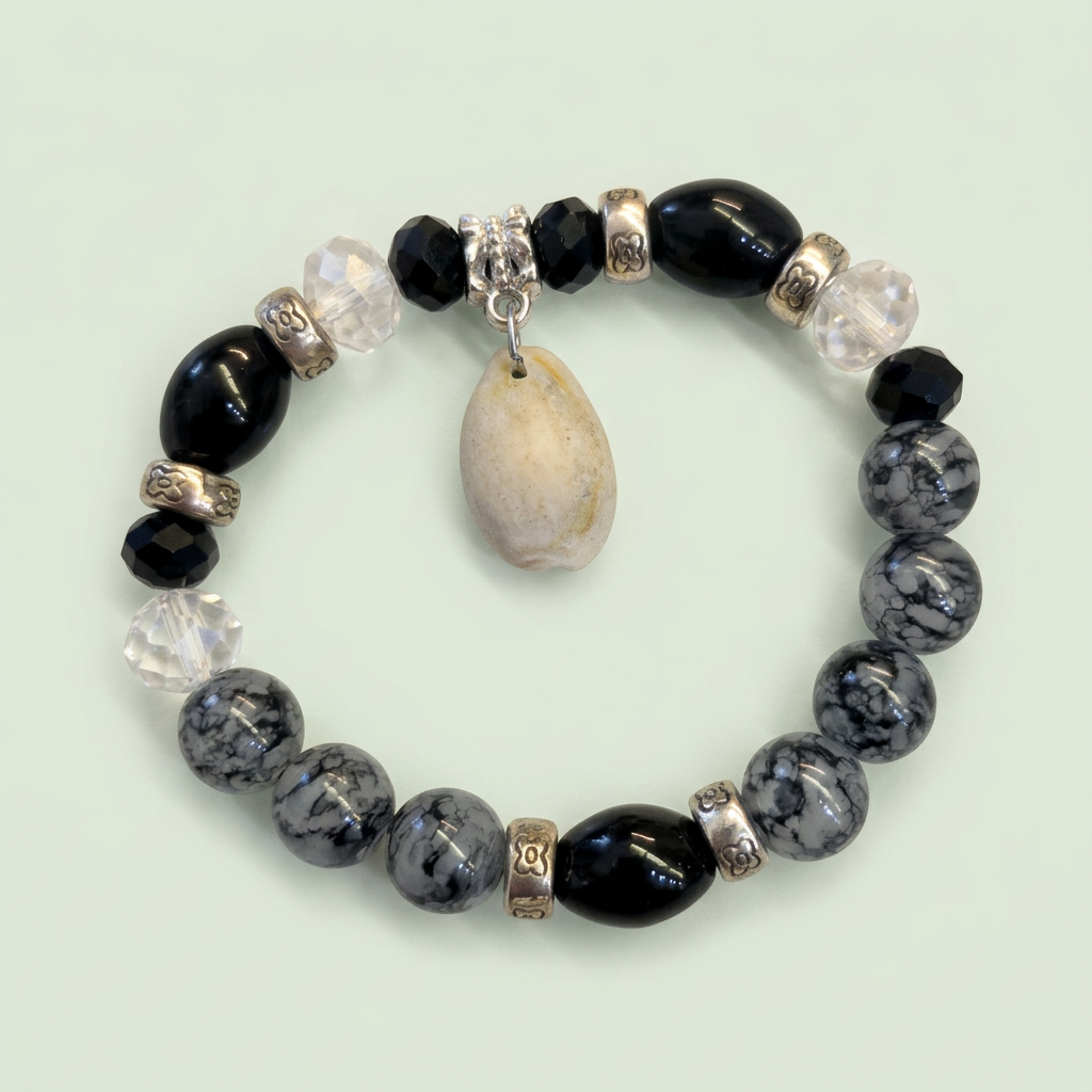 Black and gray beaded stretch bracelet with cream shell charm on a pale sage background
