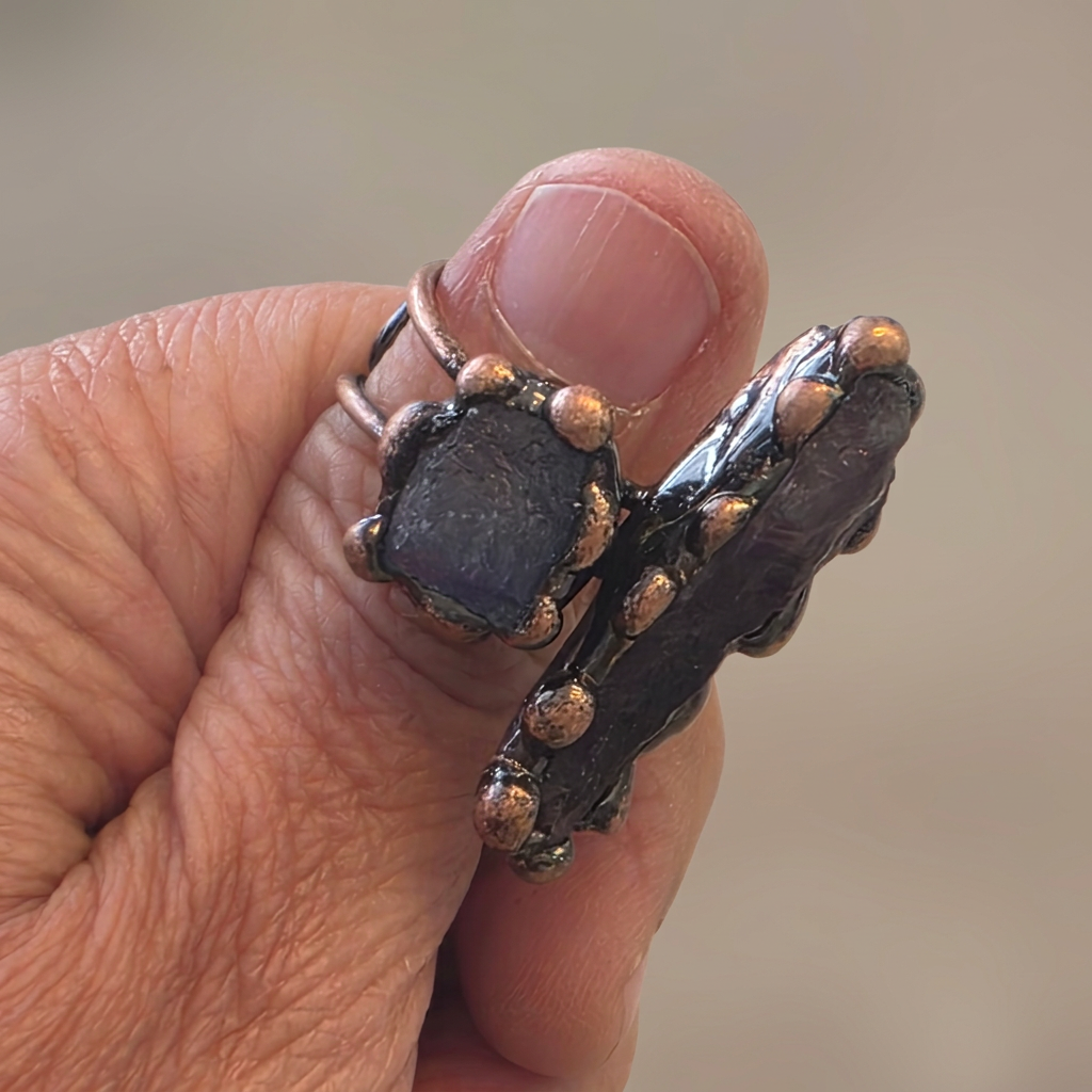 Actual amethyst and raw stone adjustable ring on a copper band, held in hand, with a cleaned and softened background