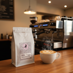 Apothecary Beans Rwanda bag in foreground with steaming latte and espresso machine in background